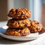 A stack of three rich, textured banana oatmeal cookies with visible chocolate chips, resting on a light plate.