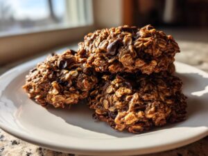 A close-up stack of three moist banana oatmeal cookies loaded with chocolate chips, sitting on a white plate.