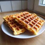 A stack of three golden brown, crispy cottage cheese waffles served on a white plate on a wooden surface.