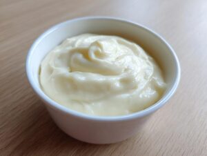 A small white bowl filled with a thick, creamy, pale yellow topping, likely sour cream or crème fraîche, for the amazing garlic soup.
