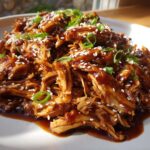 Close-up of shredded crockpot teriyaki chicken coated in rich sauce, topped with sesame seeds and green onions.