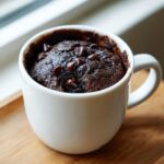 Close-up of a rich, fudgy chocolate mug cake topped with melted chocolate chips, served in a white mug.