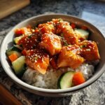 Close-up of glazed salmon cubes topped with sesame seeds in a bowl of rice and fresh vegetables, perfect for salmon bowls.