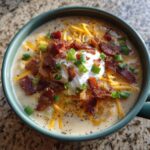 A close-up of a creamy, loaded potato soup recipe topped with bacon, cheese, sour cream, and chives.
